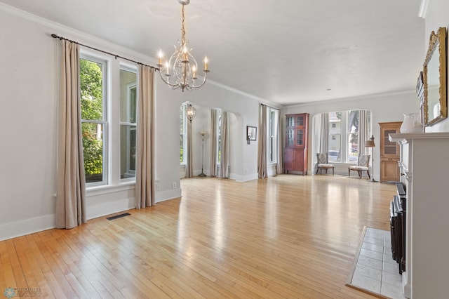 unfurnished living room with an inviting chandelier, crown molding, and plenty of natural light