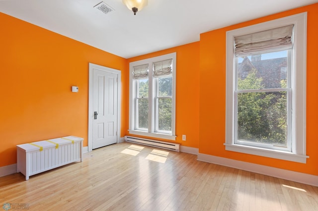 unfurnished room featuring a baseboard heating unit, a wealth of natural light, and light wood-type flooring