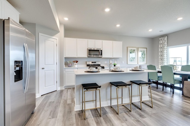 kitchen featuring light wood-type flooring, a center island with sink, white cabinets, and appliances with stainless steel finishes