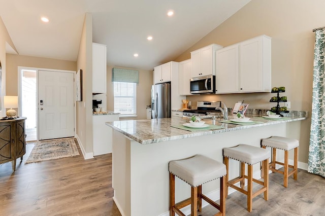 kitchen featuring white cabinetry, kitchen peninsula, stainless steel appliances, light stone countertops, and light hardwood / wood-style flooring