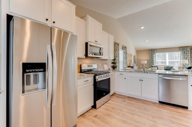 kitchen featuring appliances with stainless steel finishes, lofted ceiling, sink, white cabinets, and light stone counters