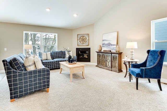 carpeted living room with lofted ceiling, baseboards, and a glass covered fireplace