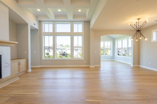 unfurnished living room with beamed ceiling, light hardwood / wood-style floors, an inviting chandelier, and plenty of natural light