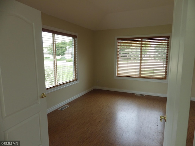 unfurnished room featuring baseboards, visible vents, and wood finished floors