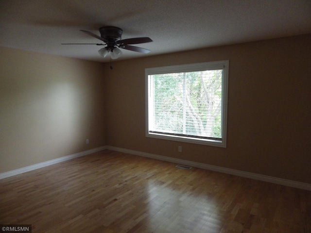 spare room featuring visible vents, ceiling fan, baseboards, and wood finished floors