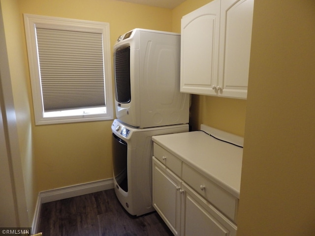 clothes washing area with dark wood-type flooring, stacked washer / dryer, cabinet space, and baseboards