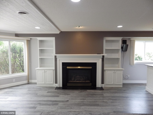 unfurnished living room featuring wood finished floors, a glass covered fireplace, visible vents, and a healthy amount of sunlight