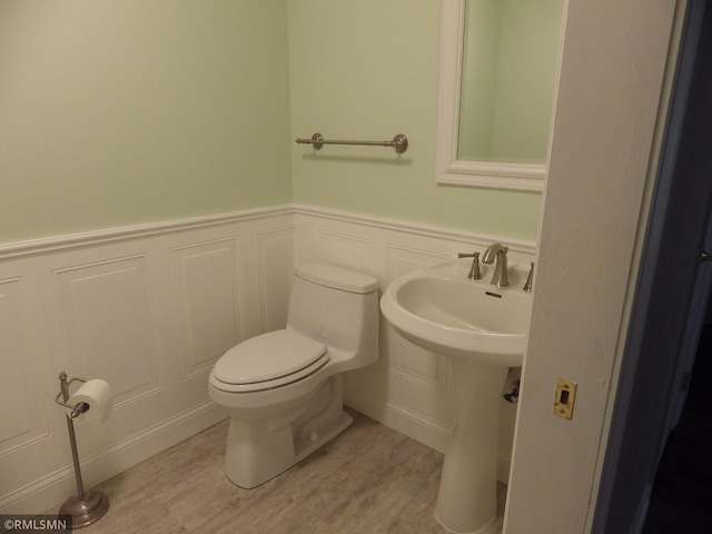 half bath featuring wainscoting, toilet, wood finished floors, a decorative wall, and a sink