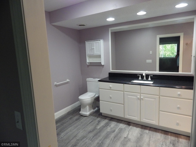 bathroom with toilet, recessed lighting, wood finished floors, vanity, and baseboards