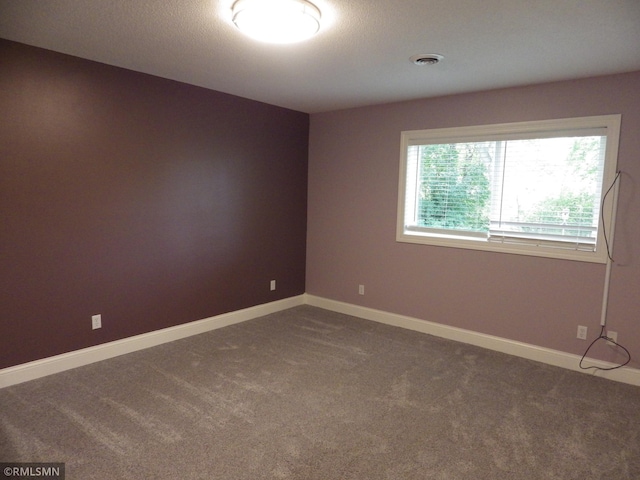 empty room featuring baseboards, visible vents, and dark carpet