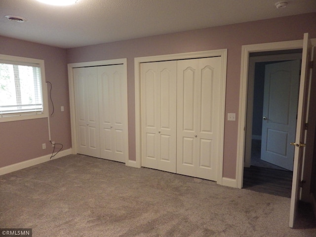 unfurnished bedroom with multiple closets, carpet, visible vents, and baseboards