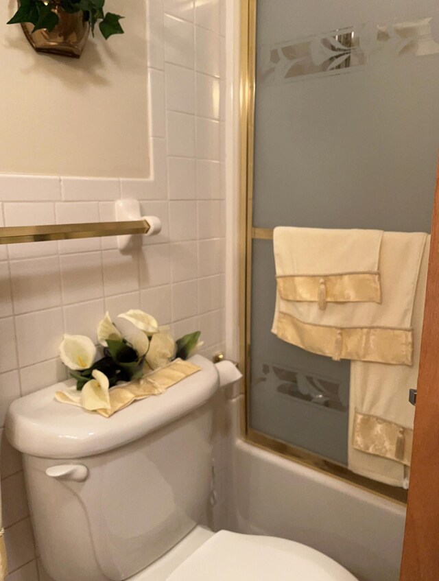 bathroom featuring tile walls, toilet, and enclosed tub / shower combo