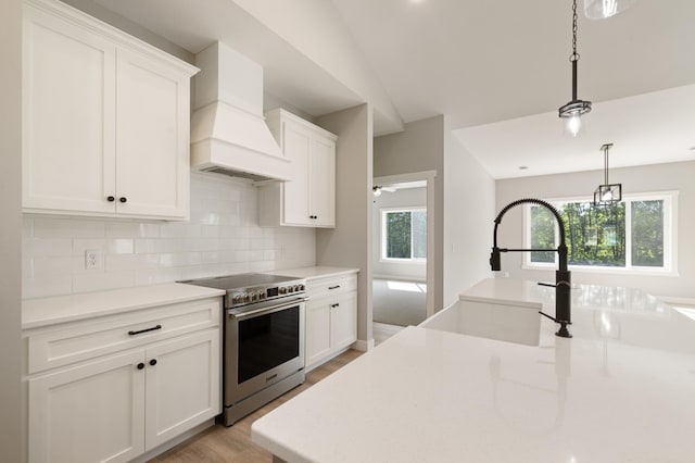 kitchen with lofted ceiling, white cabinetry, stainless steel electric range oven, decorative light fixtures, and custom exhaust hood