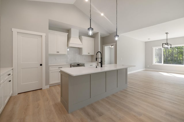 kitchen with decorative backsplash, a center island with sink, white cabinets, and premium range hood