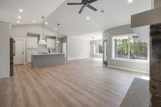 unfurnished living room with vaulted ceiling, light wood-type flooring, sink, and ceiling fan