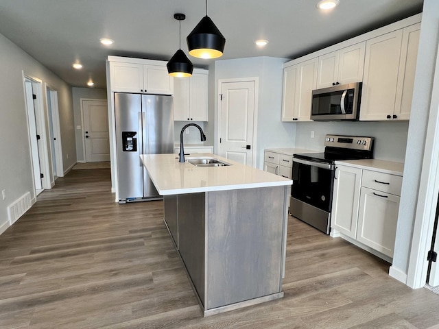 kitchen with stainless steel appliances, sink, hardwood / wood-style flooring, white cabinets, and hanging light fixtures