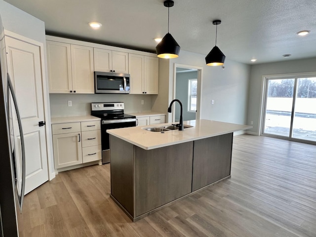 kitchen featuring a center island with sink, sink, decorative light fixtures, white cabinetry, and stainless steel appliances