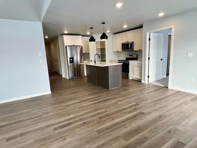 kitchen with appliances with stainless steel finishes, pendant lighting, a center island with sink, white cabinets, and hardwood / wood-style flooring