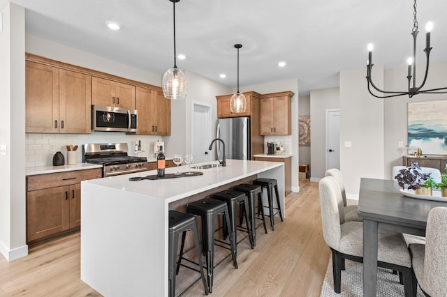 kitchen featuring an island with sink, hanging light fixtures, stainless steel appliances, and light hardwood / wood-style flooring