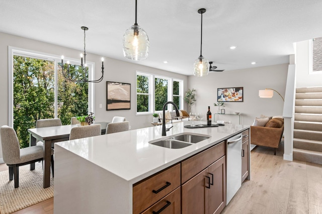 kitchen with light wood-type flooring, ceiling fan, sink, pendant lighting, and a kitchen island with sink