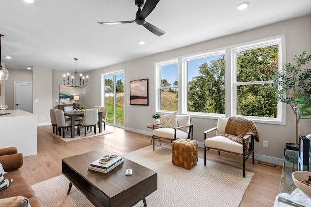 living room featuring light wood-type flooring, ceiling fan with notable chandelier, and a healthy amount of sunlight