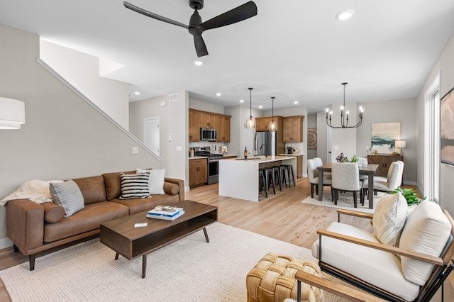 living room with light wood-type flooring and ceiling fan with notable chandelier