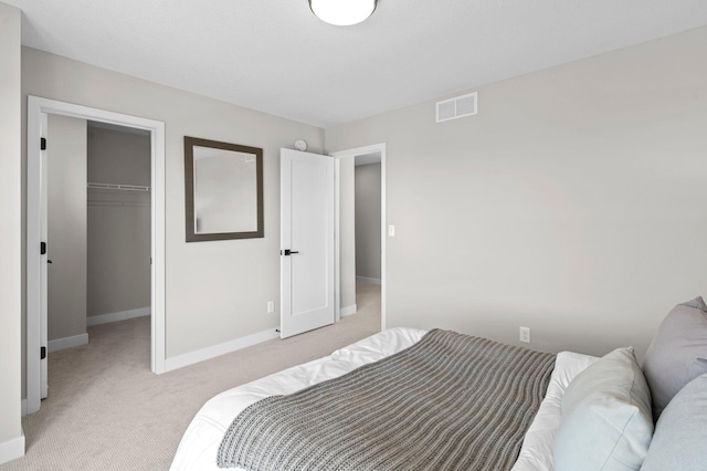 bedroom with a walk in closet, light colored carpet, and a closet