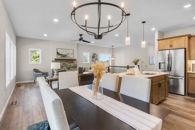 dining room with ceiling fan with notable chandelier, a fireplace, light hardwood / wood-style floors, and sink