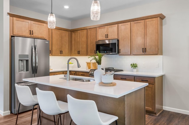 kitchen with appliances with stainless steel finishes, decorative light fixtures, sink, and a center island with sink