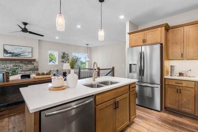 kitchen with hardwood / wood-style flooring, appliances with stainless steel finishes, sink, ceiling fan, and a center island with sink