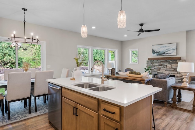 kitchen with ceiling fan with notable chandelier, a fireplace, a kitchen island with sink, stainless steel dishwasher, and sink