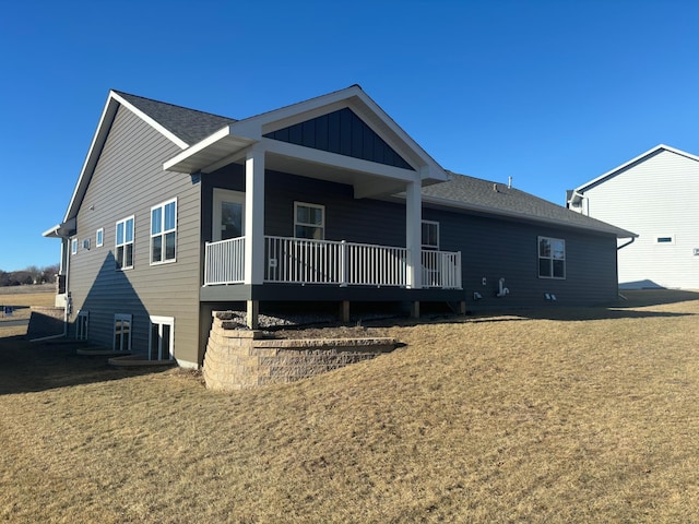 exterior space with covered porch, board and batten siding, a yard, and roof with shingles