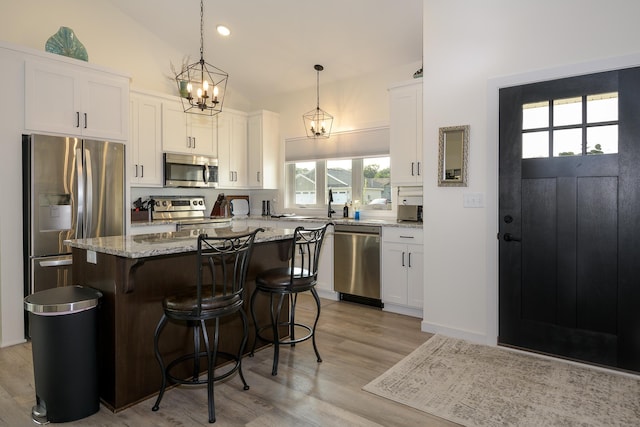 kitchen with light stone counters, decorative light fixtures, a kitchen island, stainless steel appliances, and white cabinets