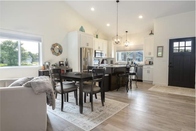 dining area with a notable chandelier, high vaulted ceiling, and light hardwood / wood-style flooring