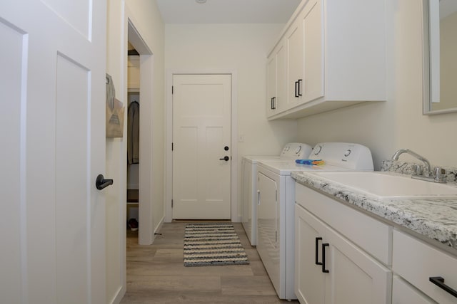 clothes washing area featuring sink, washer and clothes dryer, cabinets, and light wood-type flooring