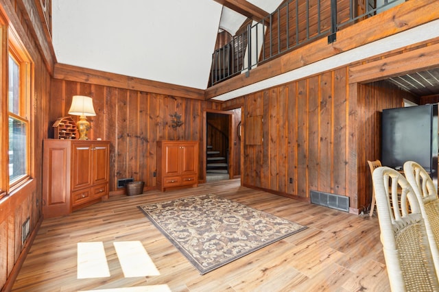 living room with light hardwood / wood-style flooring, wood walls, and high vaulted ceiling