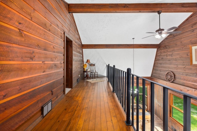 hall featuring hardwood / wood-style floors, wooden walls, and lofted ceiling with beams