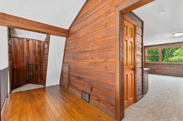 hallway with hardwood / wood-style flooring, wood walls, a textured ceiling, and vaulted ceiling