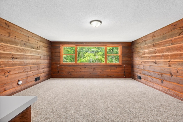 carpeted empty room with a textured ceiling and wood walls