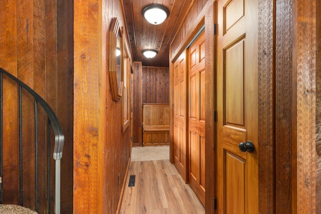 corridor with light hardwood / wood-style floors, wood ceiling, and wood walls