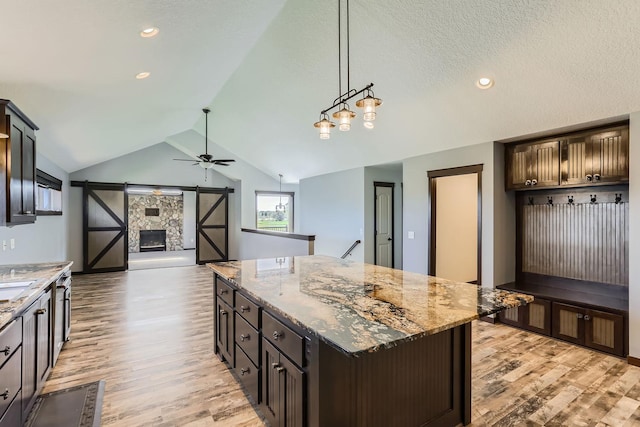 kitchen featuring dark brown cabinetry, light stone counters, a kitchen island, light hardwood / wood-style flooring, and vaulted ceiling