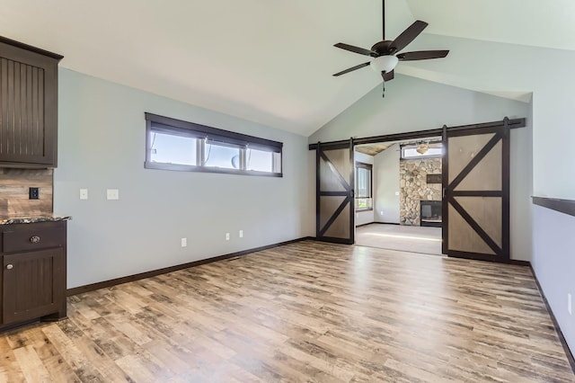 interior space featuring ceiling fan, light wood-type flooring, a barn door, and lofted ceiling