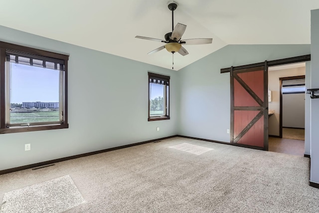 empty room with ceiling fan, vaulted ceiling, plenty of natural light, and a barn door