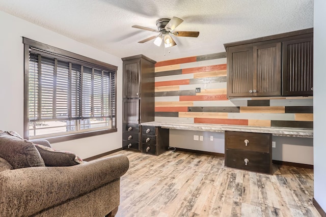 office with ceiling fan, a textured ceiling, light hardwood / wood-style flooring, and built in desk