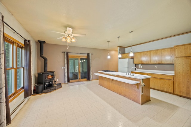 kitchen with a wood stove, hanging light fixtures, white appliances, a center island with sink, and ceiling fan