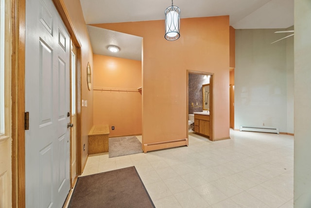hall with baseboard heating, light tile patterned flooring, a sink, baseboards, and high vaulted ceiling