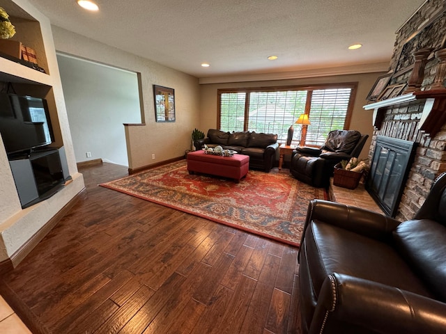 living room with a stone fireplace, a textured ceiling, and wood-type flooring