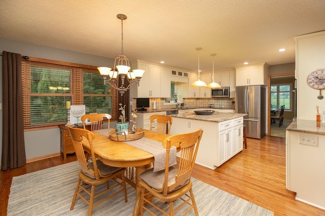 dining area with sink, a textured ceiling, a chandelier, and light hardwood / wood-style flooring