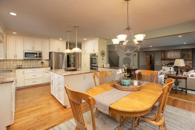 dining area featuring a large fireplace, a textured ceiling, a notable chandelier, light wood-type flooring, and sink