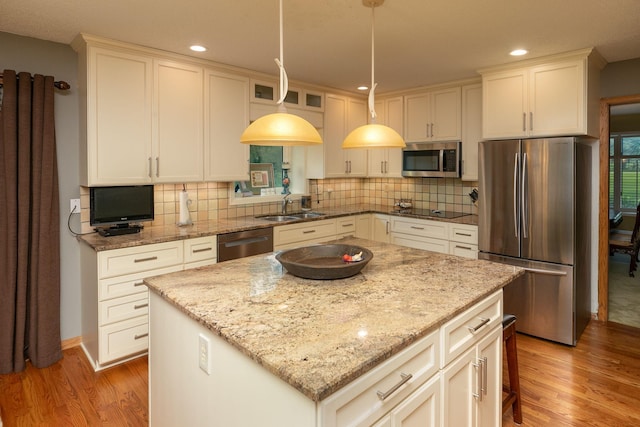 kitchen featuring light stone counters, decorative light fixtures, stainless steel appliances, a kitchen island, and sink